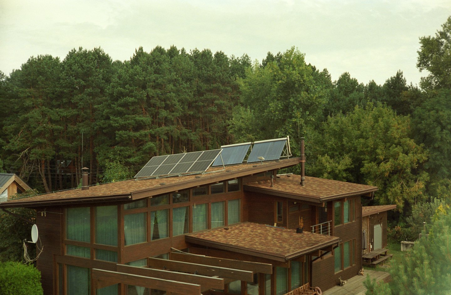 Modern wooden house with solar panels on a forest-backed roof.